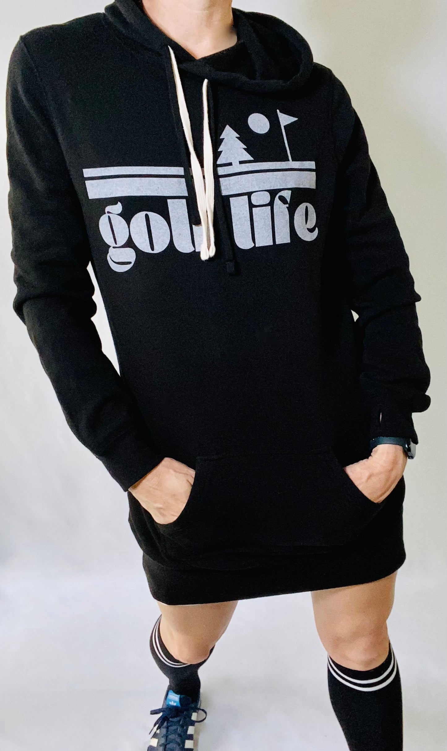 This is a photograph of a woman wearing a black, hooded sweatshirt dress. She's wearing black knee high socks. The sweatshirt features a bold design that says "Golf Life"