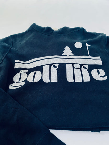 This is an up-close photo of the screen print design on a hooded sweatshirt dress. It says golf life and features an evergreen tree, sun and golf flag.