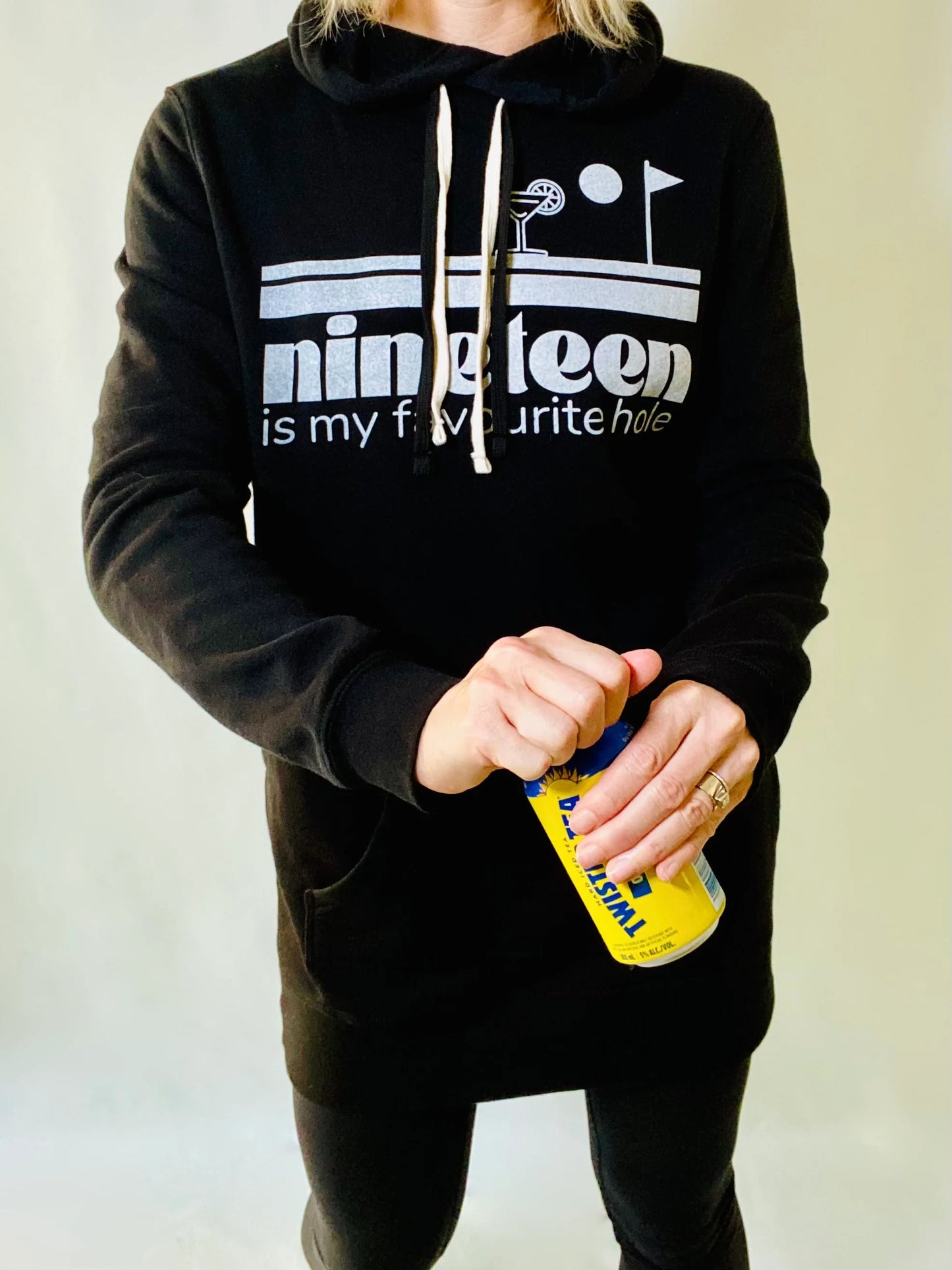 A woman wearing a Nineteenth hole sweatshirt dress by Golf Garter holding a beverage.